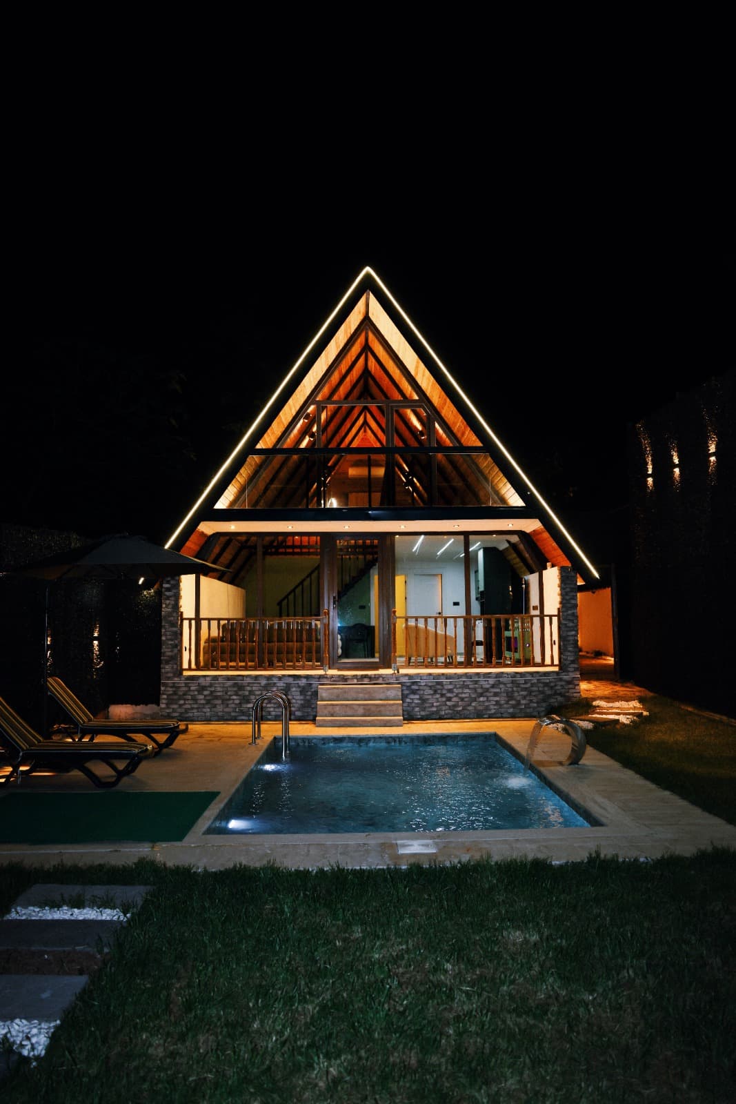 Bahçe ve havuzuyla gece aydınlatmalı A-frame bungalov genel görünüm