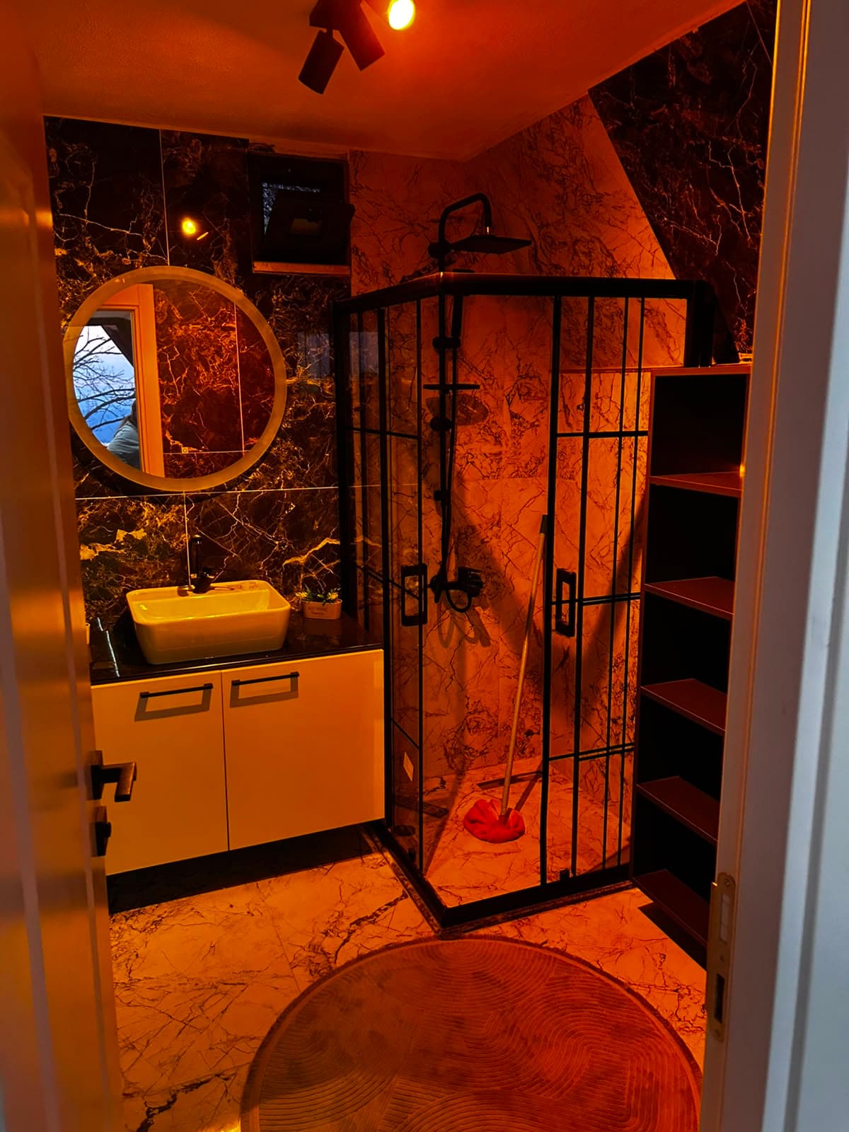 Mermer dokulu modern banyo, siyah çerçeveli duşakabin ve yuvarlak ayna