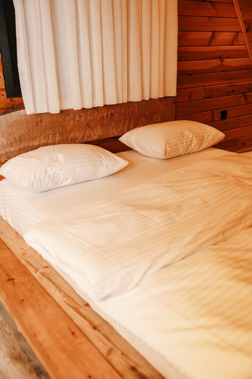 Yatak başlığındaki Sapanca Jilon Villa oyması ve pamuklu nevresim detayı